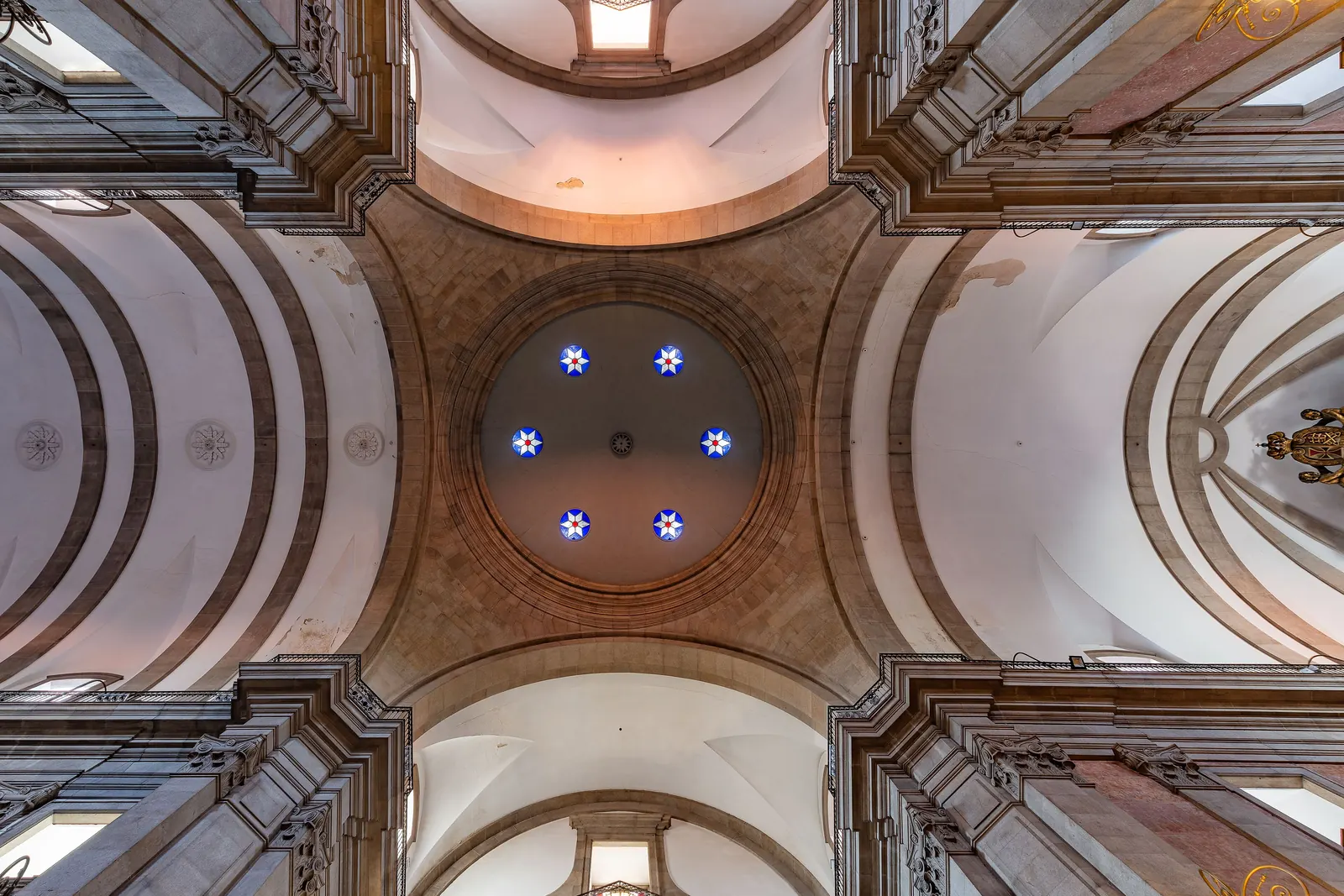 Looking straight up into the white and gilded vaulted ceiling of the Trindade church, with a ring of small blue stars at its centre