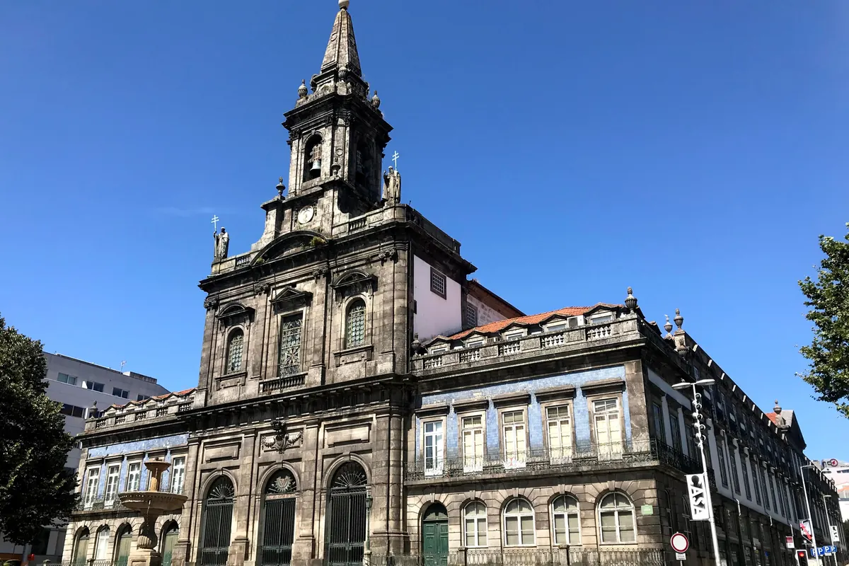 The granite front and clock tower of the Trindade church in Porto seen from the square under a blue sky