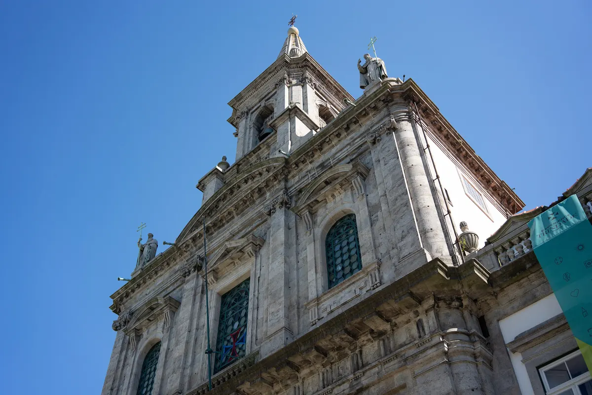 The pale stone front of a baroque-style church in Porto seen from below against a blue sky