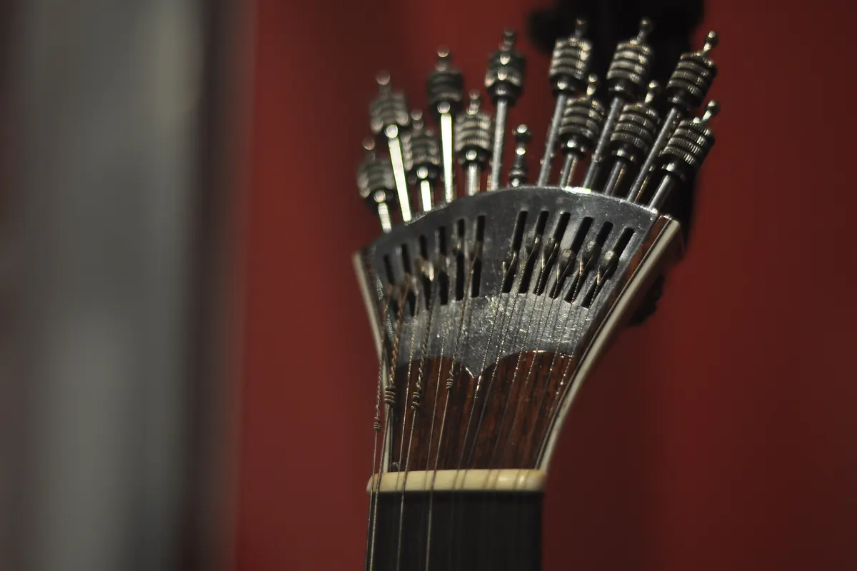 Close view of the metal watch-key tuning pegs of a Portuguese guitar against a red background